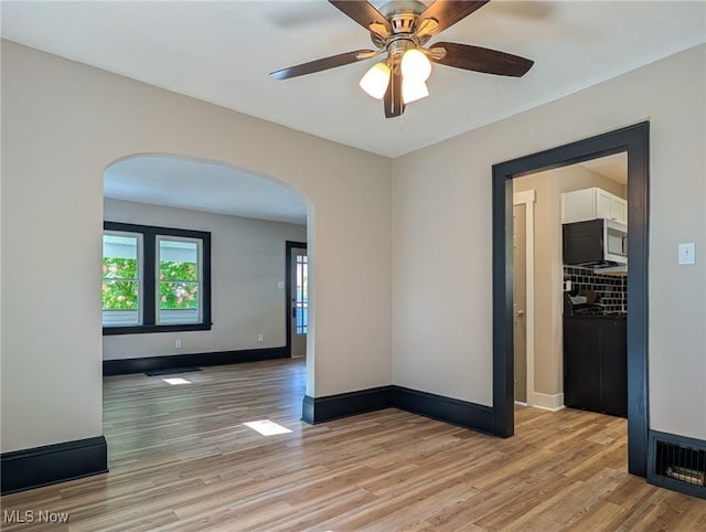 unfurnished room with arched walkways, light wood-style flooring, and baseboards