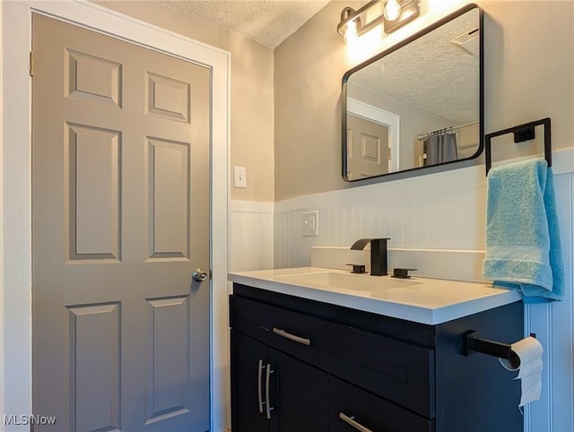 bathroom with a textured ceiling, a wainscoted wall, and vanity