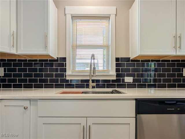 kitchen with stainless steel dishwasher, a sink, white cabinets, tasteful backsplash, and light countertops