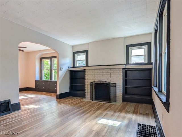 unfurnished living room featuring wood finished floors, arched walkways, a brick fireplace, and baseboards