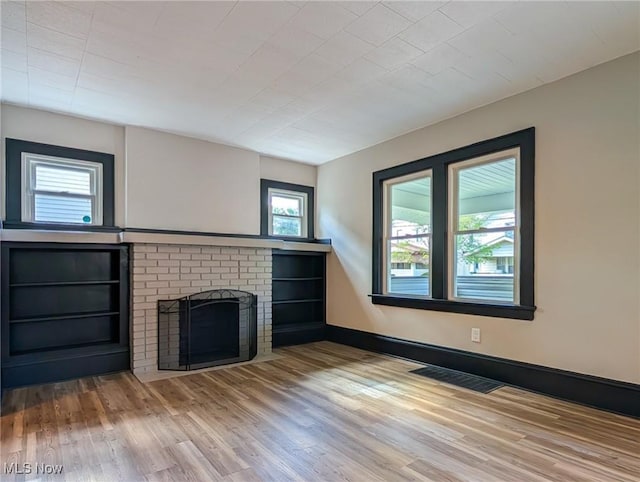 unfurnished living room with wood finished floors, a brick fireplace, and baseboards