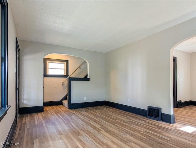 unfurnished room with arched walkways, wood finished floors, baseboards, and stairs
