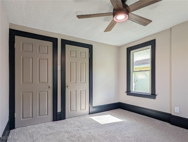 unfurnished bedroom with carpet flooring, a textured ceiling, a ceiling fan, and baseboards