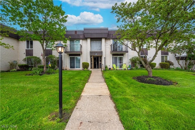 view of front of house featuring a balcony, brick siding, and a front yard