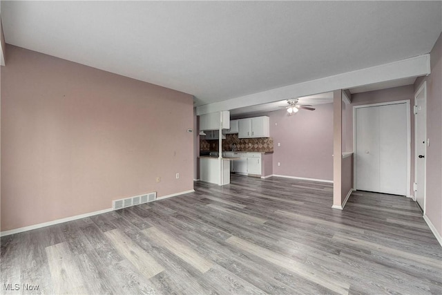 unfurnished living room featuring a ceiling fan, wood finished floors, and baseboards