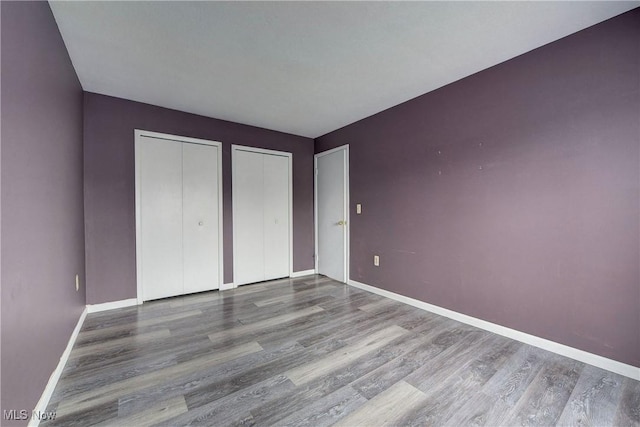 unfurnished bedroom with multiple closets, wood finished floors, and baseboards