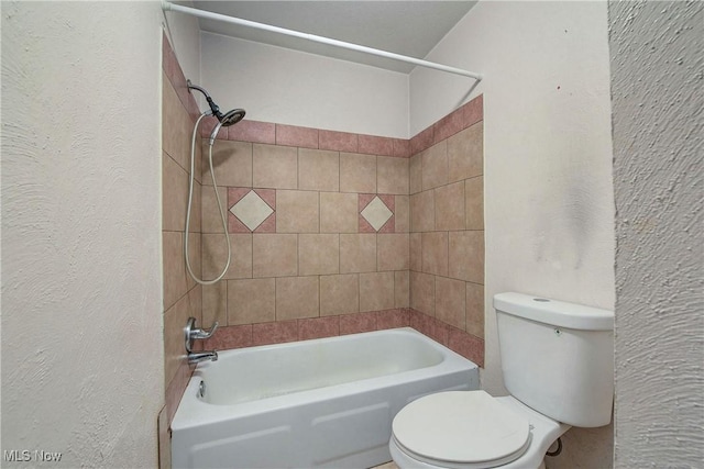 bathroom featuring toilet, a textured wall, and shower / bathtub combination