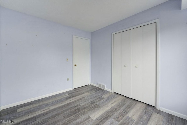 unfurnished bedroom with wood finished floors, baseboards, and a closet