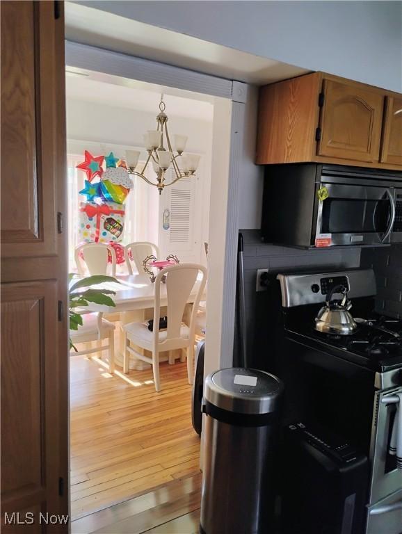 13418 Coath Ave, Cleveland, OH 44120 - kitchen featuring stainless steel gas stove, a chandelier, light wood finished floors, hanging light fixtures, and brown cabinetry