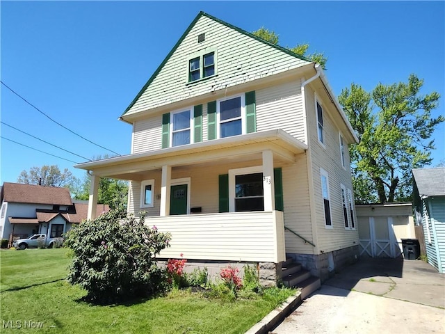 american foursquare style home with covered porch, a front yard, and an outbuilding
