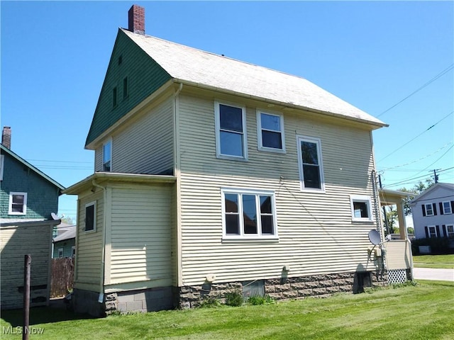 back of property with a chimney and a lawn
