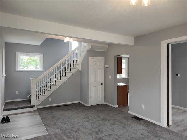 unfurnished living room featuring stairs, baseboards, carpet floors, and a textured ceiling