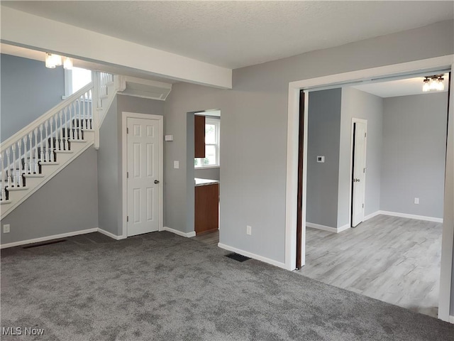 unfurnished living room featuring stairs, baseboards, and carpet flooring