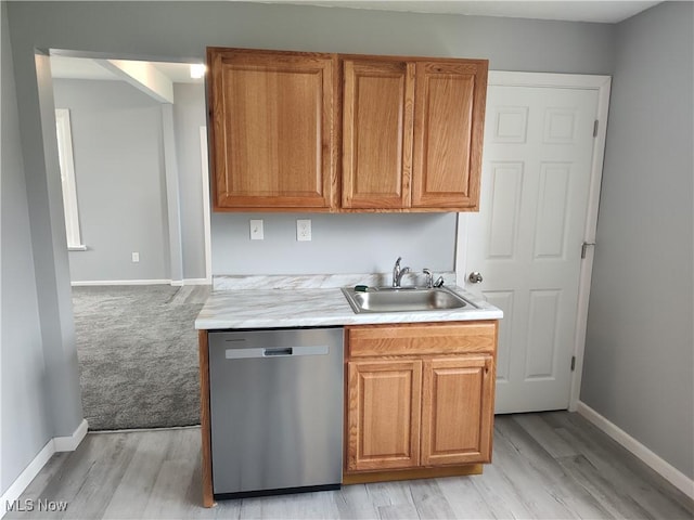 kitchen featuring stainless steel dishwasher, a sink, baseboards, light countertops, and light wood finished floors