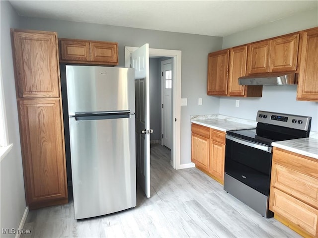 kitchen with stainless steel appliances, under cabinet range hood, light wood finished floors, and light countertops