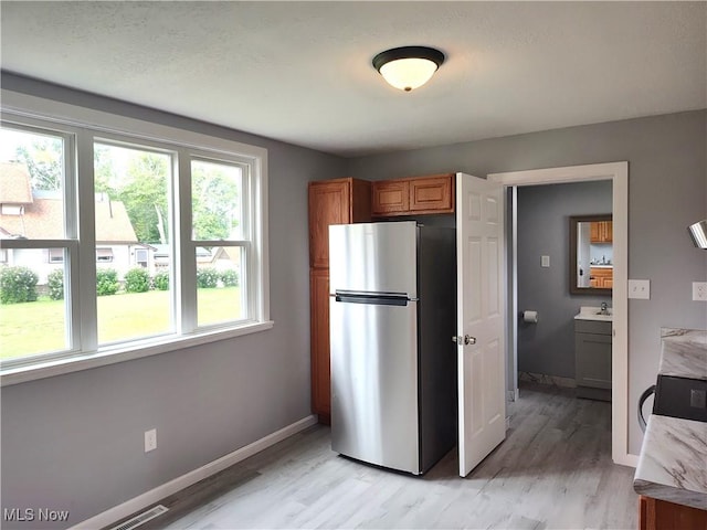 kitchen featuring freestanding refrigerator, light wood finished floors, brown cabinetry, baseboards, and range