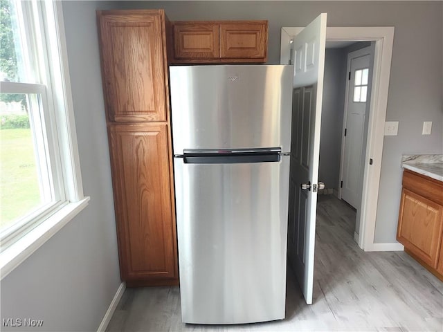 kitchen with freestanding refrigerator, baseboards, brown cabinetry, and light wood finished floors