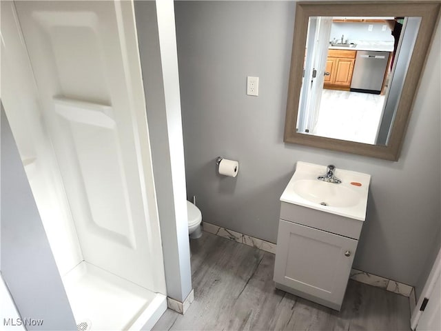 bathroom with wood finished floors, vanity, a shower stall, toilet, and baseboards