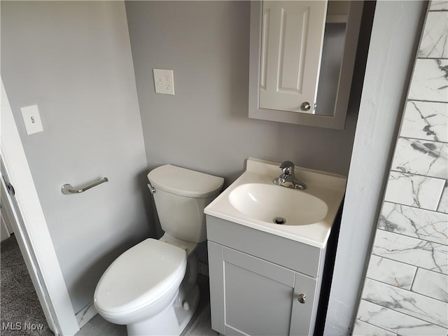 half bath with marble finish flooring, vanity, and toilet