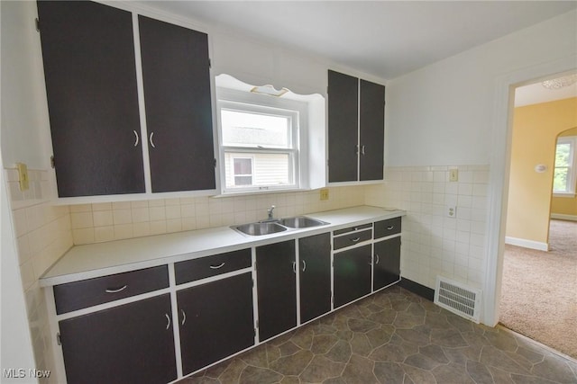 kitchen featuring a sink, dark carpet, light countertops, tile walls, and arched walkways