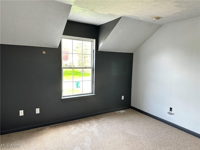 additional living space featuring a textured ceiling, carpet, vaulted ceiling, and baseboards