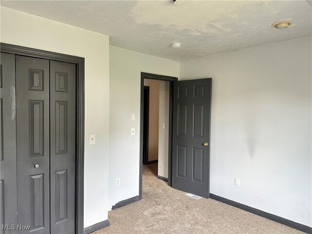 unfurnished bedroom with light carpet, baseboards, a closet, and a textured ceiling