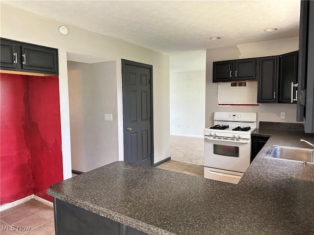 kitchen featuring white range with gas cooktop, a sink, dark countertops, baseboards, and a textured ceiling