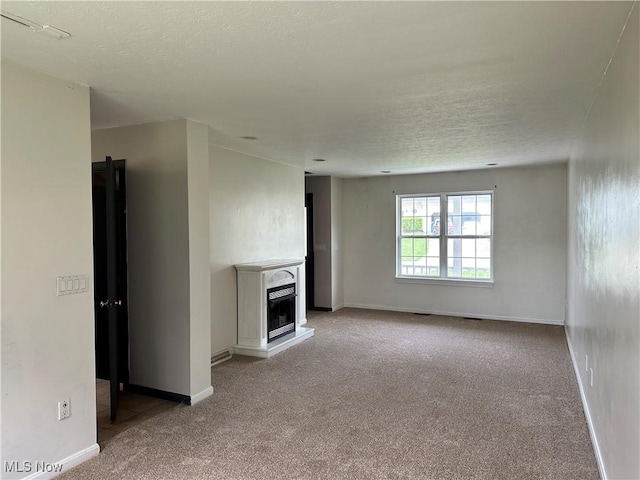 unfurnished living room with carpet floors, a fireplace with raised hearth, a textured ceiling, and baseboards