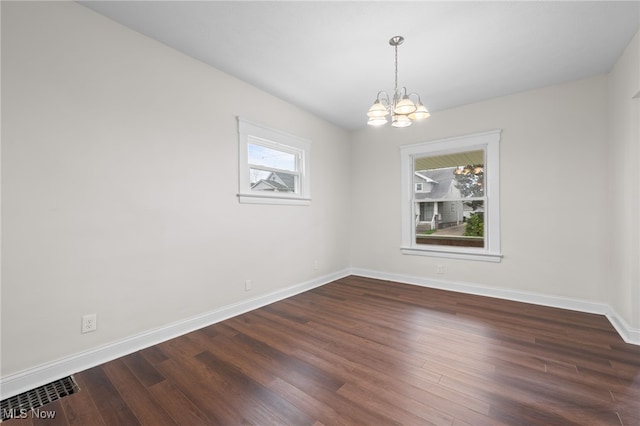 spare room with a chandelier, baseboards, and dark wood-style flooring