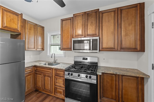 kitchen featuring appliances with stainless steel finishes, a sink, dark wood-type flooring, light stone countertops, and brown cabinets