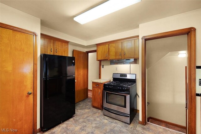 6119 E Sprague Rd, Independence, OH 44131 - kitchen featuring stainless steel gas stove, freestanding refrigerator, under cabinet range hood, brown cabinets, and light countertops