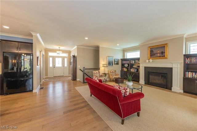 living room with crown molding, a glass covered fireplace, light wood-style floors, recessed lighting, and baseboards