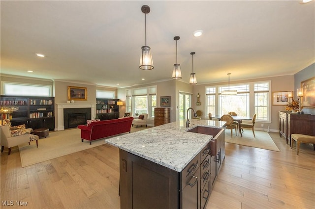kitchen with crown molding, a sink, light wood-style flooring, a glass covered fireplace, and light stone counters