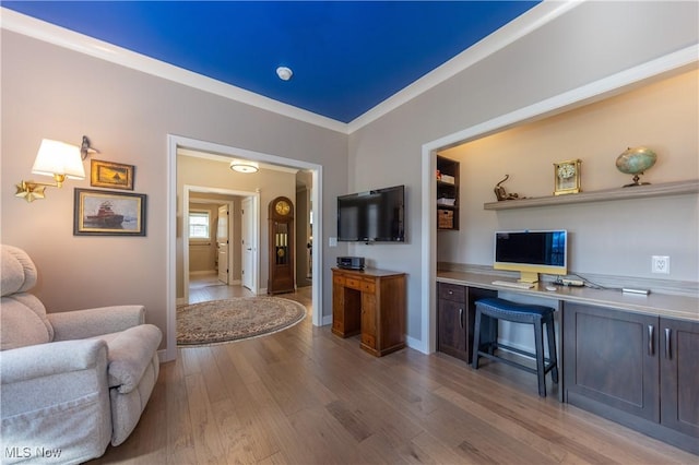 office area with wood finished floors, baseboards, ornamental molding, and built in desk