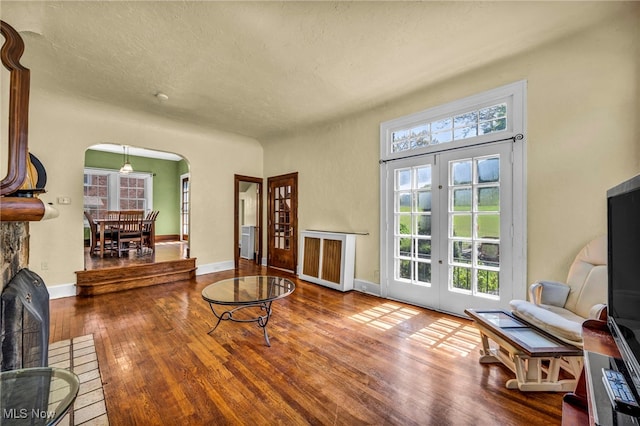 living area featuring arched walkways, radiator, french doors, wood finished floors, and baseboards
