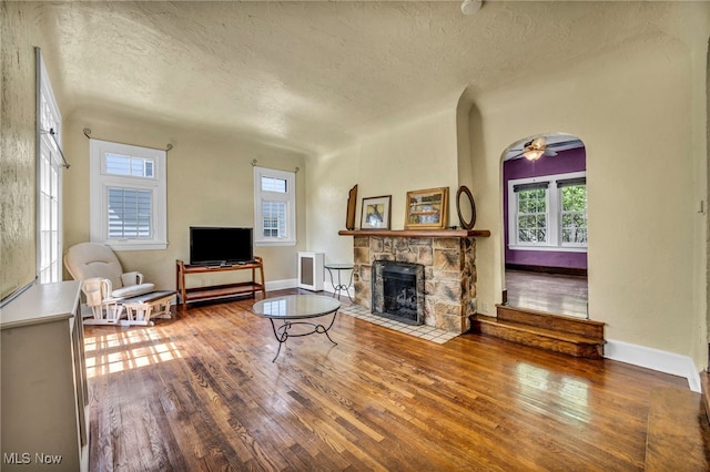 living area featuring a textured ceiling, wood finished floors, healthy amount of natural light, and a stone fireplace