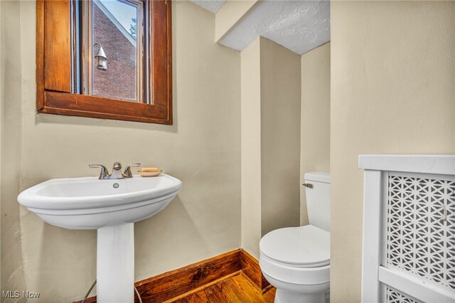 half bath with toilet, wood finished floors, baseboards, and a sink