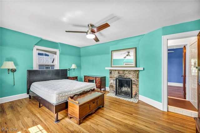 bedroom with baseboards, wood finished floors, a fireplace, and a ceiling fan