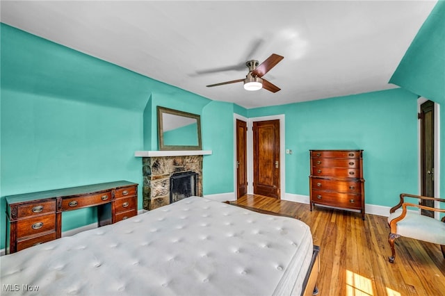 bedroom featuring wood finished floors, baseboards, a fireplace, and ceiling fan
