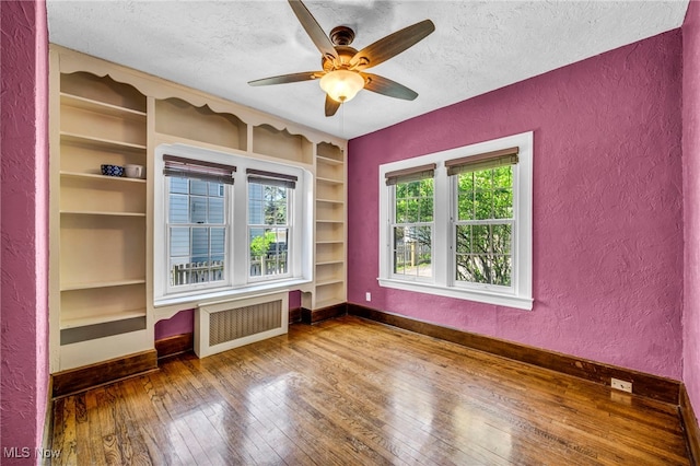 unfurnished room featuring radiator, a textured wall, a textured ceiling, built in features, and baseboards