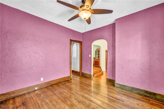 spare room with arched walkways, wood finished floors, ceiling fan, a textured wall, and baseboards