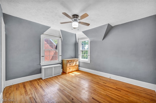 bonus room featuring radiator heating unit, baseboards, a textured ceiling, wood-type flooring, and ceiling fan