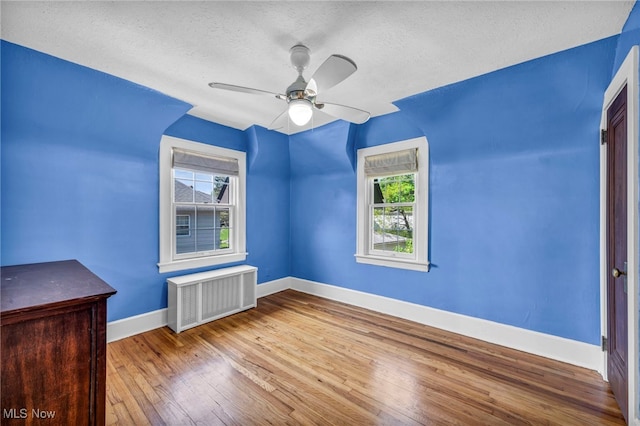 unfurnished room with radiator heating unit, plenty of natural light, baseboards, wood finished floors, and a textured ceiling