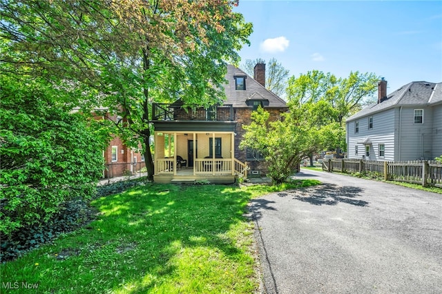 back of property featuring covered porch, a balcony, a chimney, and asphalt driveway