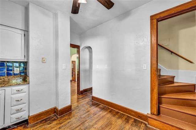interior space featuring arched walkways, dark wood-style flooring, baseboards, and stairs