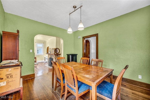dining area with arched walkways, dark wood-style floors, baseboards, and a fireplace