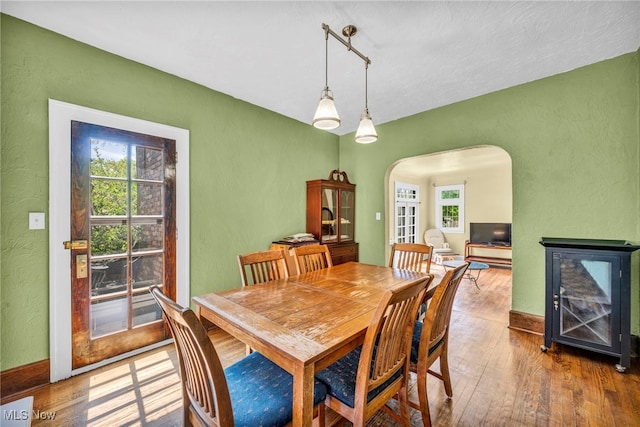 dining area with a textured wall, arched walkways, hardwood / wood-style floors, and baseboards
