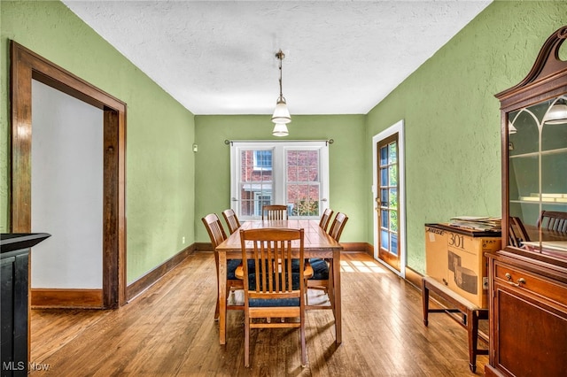 dining room featuring a textured wall, wood-type flooring, a textured ceiling, healthy amount of natural light, and baseboards
