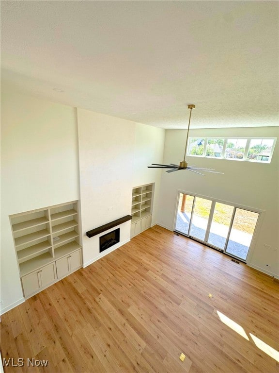 2702 Rocky Ridge Dr, Westlake, OH 44145 - unfurnished living room with light wood finished floors, ceiling fan, a fireplace, built in shelves, and baseboards