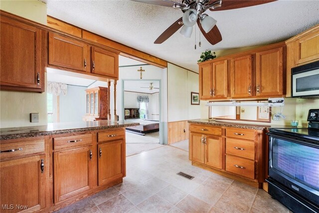 9493 State Route 9, Hanoverton, OH 44423 - kitchen featuring black range with electric stovetop, stainless steel microwave, ceiling fan, brown cabinets, and dark stone countertops